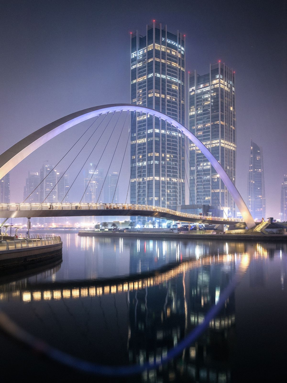 Ponte iluminada e arranha-céus refletidos na água à noite